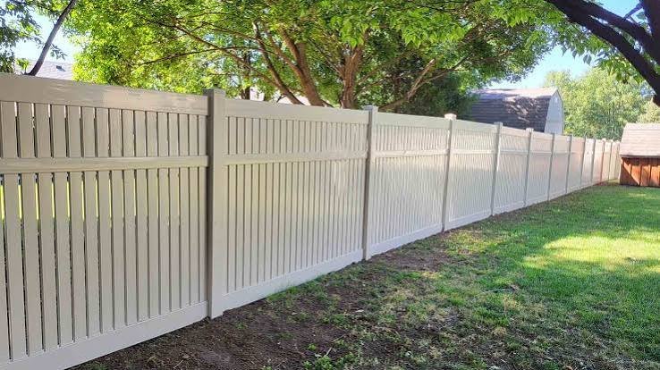 Tan vinyl semi-privacy fence along a backyard