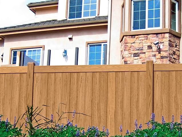 Wood-grain vinyl privacy fence in front of a stucco home